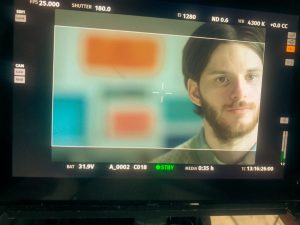 Behind the scenes image from The Phoney of a camera monitor showing the lead actor Sam Hume. The monitor is overlaid with labels of camera settings