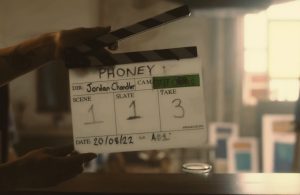 An on set image from short film The Phoney depicting a clapper board with the title and scene numbers written on it.